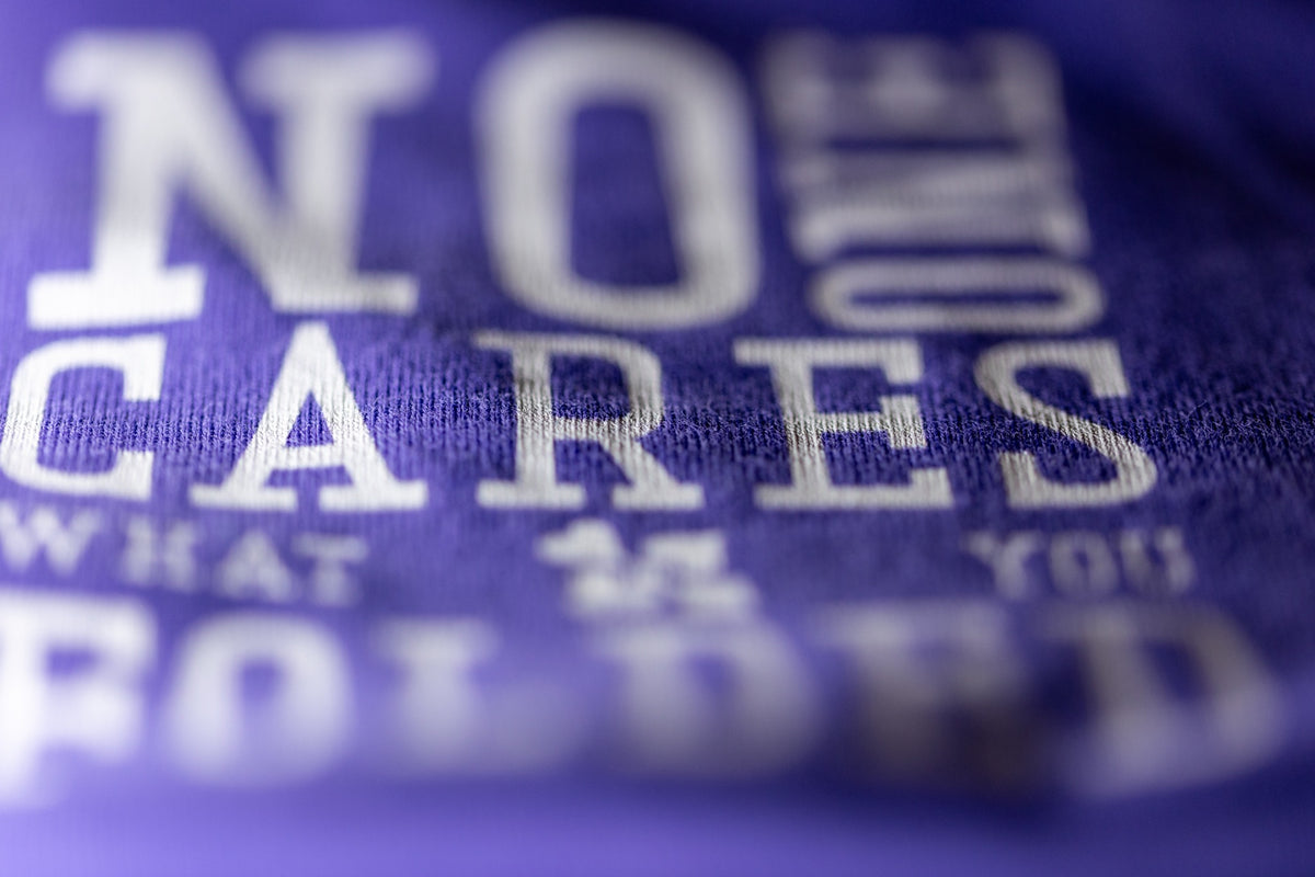 Close-up print detail of NO ONE CARES WHAT YOU FOLDED on purple poker T-shirt