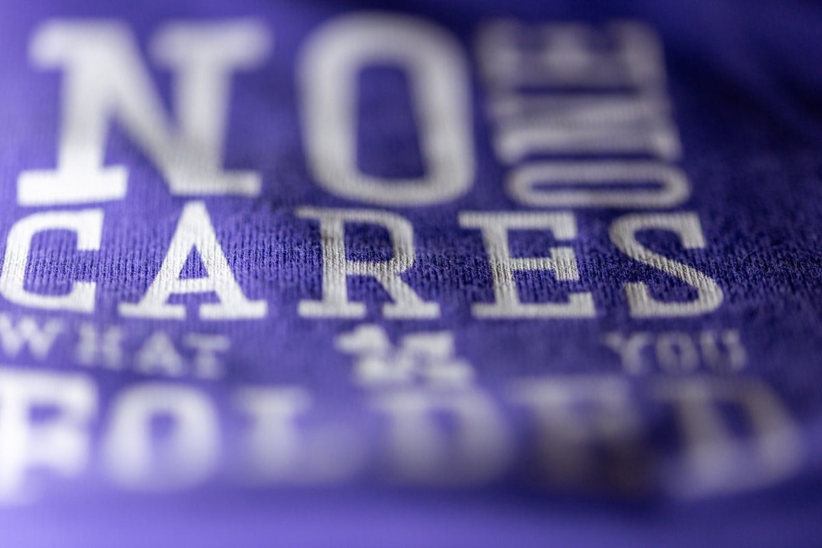 Close-up print detail of NO ONE CARES WHAT YOU FOLDED on purple poker T-shirt